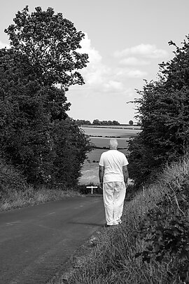 Black and white image of a man stood at the top of a countryside hill looking down it 