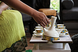 A hand reaching for a coffee pot to pour coffee into cups laid out on a table