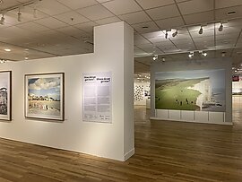 A photograph of an exhibition with photographs in frames hanging on temporary walls 