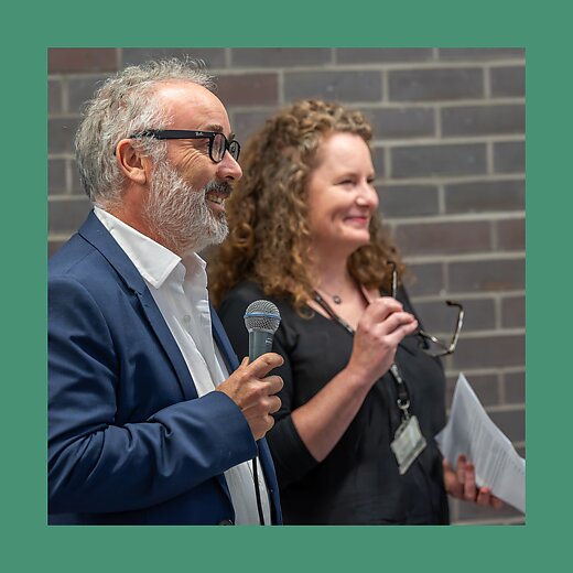 A close up of man and woman smiling and talking, the man has amicrophone in hand