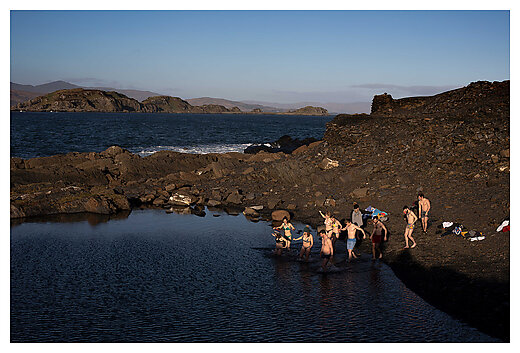 men and women in swimwear getting into natural water amongst rocky hills