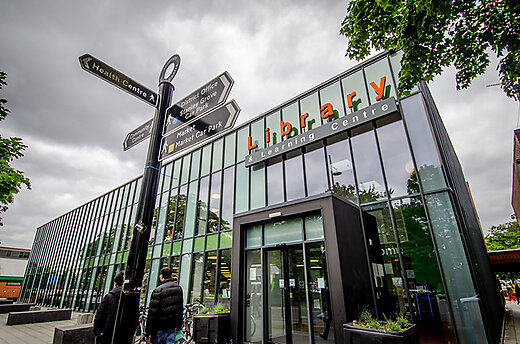 Front of library with its sign and pedestrian pathway signs to other local places